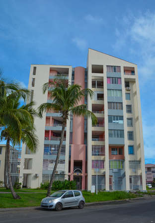 Point-a-Pitre, Guadeloupe - Sept 17, 2018: Colorful residential building of local people on the street with green palm trees, road and a parked carのeditorial素材