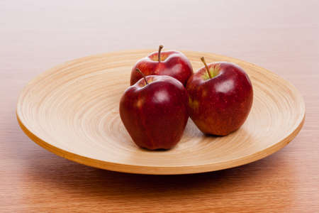 three red apples on a wooden plateの写真素材