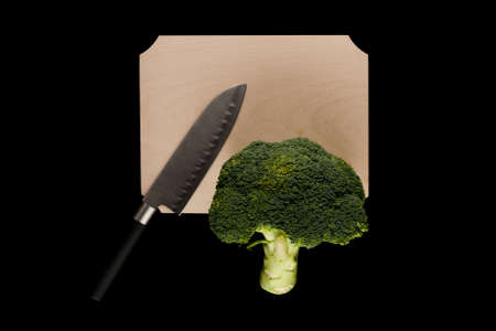 broccoli with knife on wooden cutting board on black backgroundの写真素材