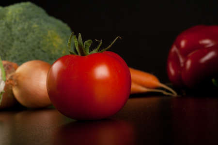 tomato on black with different vegetables in the backgroundの写真素材