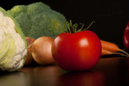 tomato on black with different vegetables in the backgroundの写真素材