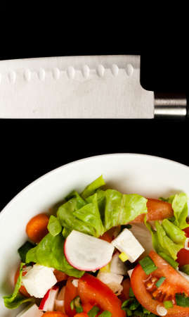vegetable salad in a white bowl with big knife on black backgroundの写真素材