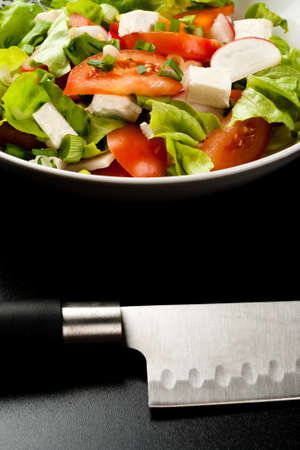 vegetable salad in a white bowl with big knife on black backgroundの写真素材