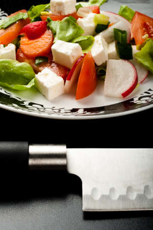 vegetable salad in a white bowl with big knife on black backgroundの写真素材