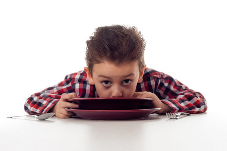 young boy slurping soup out of a marsala color plateの写真素材