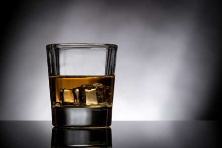 back lit whisky glass with ice and reflectionの写真素材