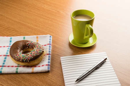 doughnut coffee and notepad with pen on a tableの写真素材