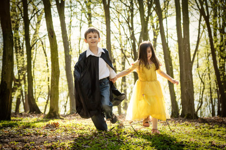 boy with black cape and girl in yellow princess dress in forest