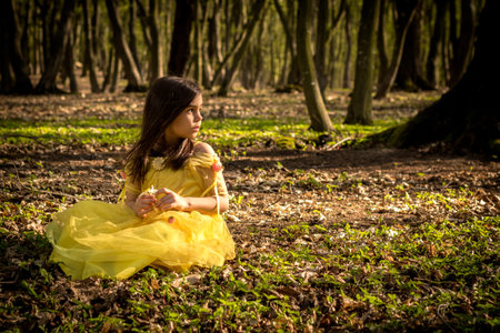 little girl in yellow princess dress in forestの写真素材