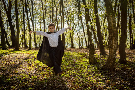 little boy with black cape in forest