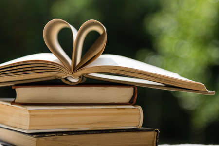 stack of books on table in garden with top one opened and pages forming heart shapeの写真素材