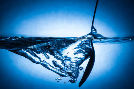 spoon making waves in fresh water with blue backgroundの写真素材