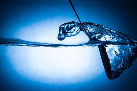 spoon making waves in fresh water with blue backgroundの写真素材