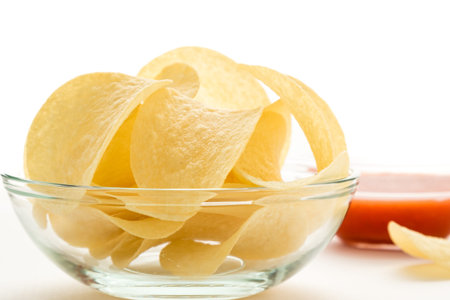 potato chips in a glass bowl on a white table with tomato dip