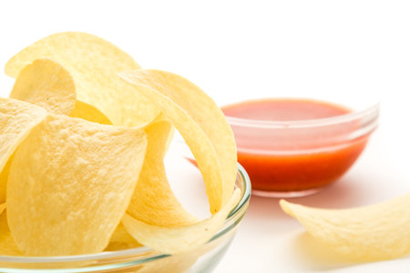 potato chips in a glass bowl on a white table with tomato dip