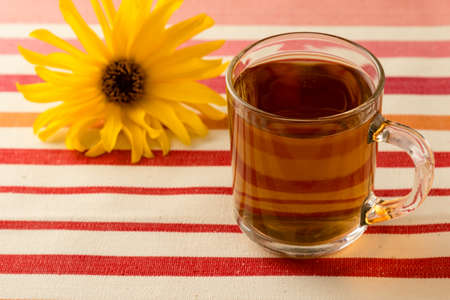 fresh black tea in a glass mug with yellow flower on tableの写真素材