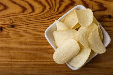 potato chips in a white bowl on a wooden tableの写真素材