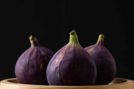 three natural ripe figs on a wooden plate
