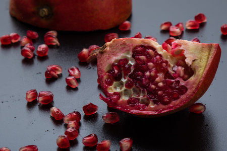 cut pomegranate and seeds on a black tableの写真素材