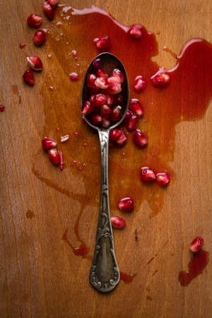 juicy pomegranate seeds in a spoon on a wooden tableの写真素材