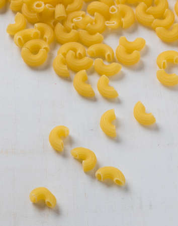 raw uncooked yellow macaroni on white wooden table