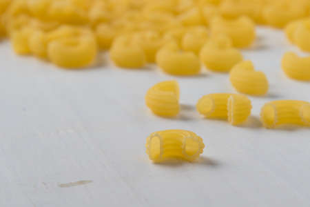 raw uncooked yellow macaroni on white wooden table