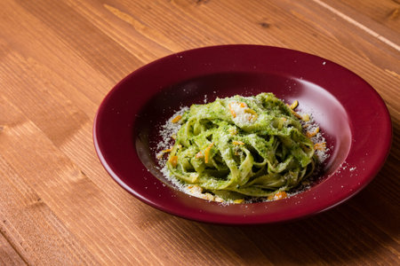 fresh green vegetarian tagliatelle dish in red plate on wooden tableの写真素材