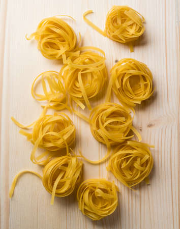 raw dry yellow tagliatelle pasta on wooden tableの写真素材