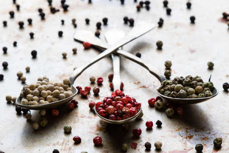 different color peppercorn seeds on vintage spoons on steel plate