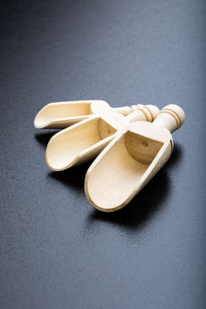 three Small and large wooden spice scoops on black tableの写真素材