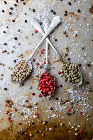 different color peppercorn seeds on vintage spoons on steel plateの写真素材