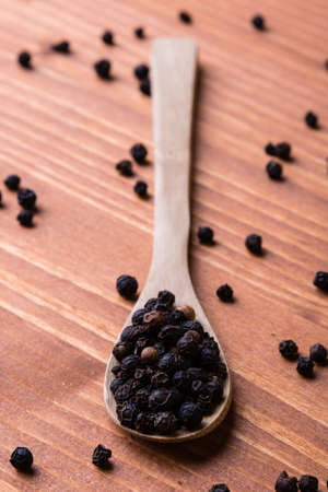 black color peppercorn seeds on wooden table with spoon