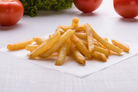 fresh yellow fries on white table with vegetables