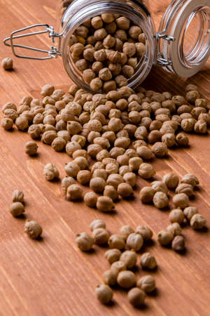 dry brown chickpeas in glass jar on wooden tableの写真素材