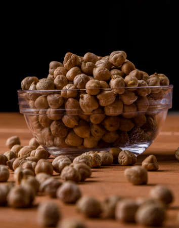 dry brown chickpeas in a glass bowl on wooden tableの写真素材