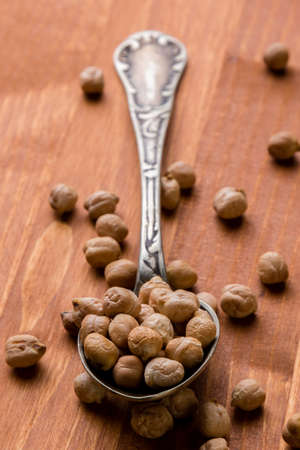dry brown chickpeas on wooden table with spoonの写真素材
