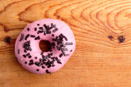 donut with pink frosting on wooden tableの写真素材