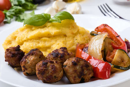 polenta with meatballs and fried vegetables on a white plateの写真素材