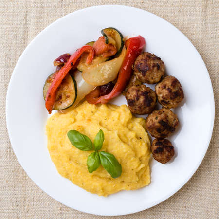polenta with meatballs and fried vegetables on a white plateの写真素材
