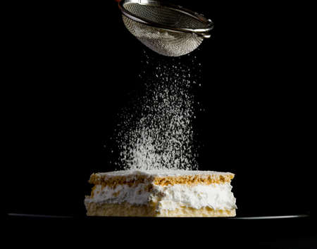 Cream pie with layers of puff pastry being sprinkled with powdered sugarの写真素材