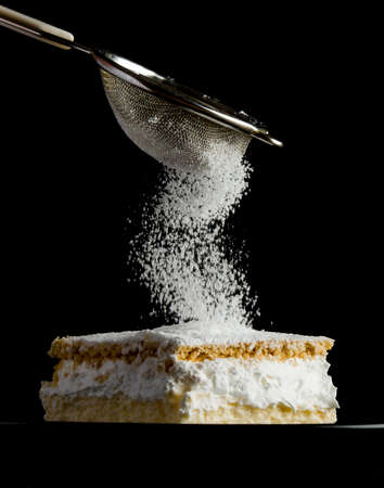 Cream pie with layers of puff pastry being sprinkled with powdered sugarの写真素材