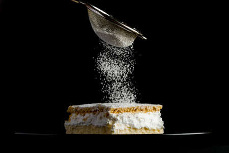 Cream pie with layers of puff pastry being sprinkled with powdered sugarの写真素材