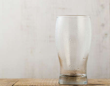 empty beer glass with water droplets on wooden tableの写真素材