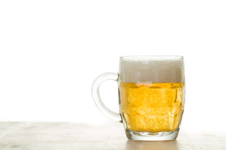 fresh cold glass of beer with foam on white wooden tableの写真素材