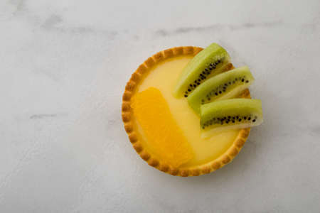 round vanilla tart with kiwi and orange on tableの写真素材