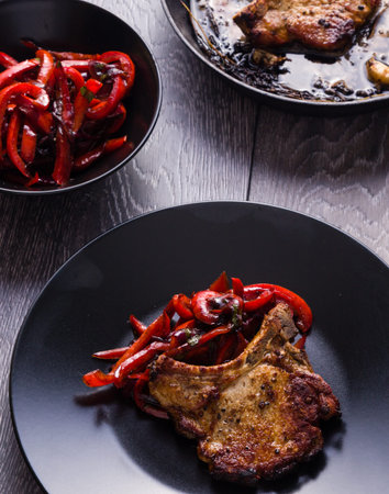 Pan fried pork chops with peppers on black plateの写真素材