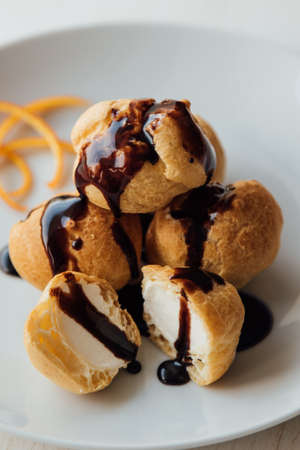 Tasty profiteroles with cream and chocolate glaze on a plateの写真素材