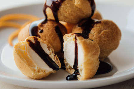 Tasty profiteroles with cream and chocolate glaze on a plateの写真素材