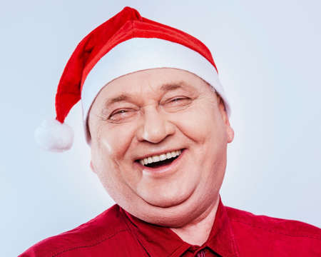 Close up portrait of laughing out loud middle aged man with red Santa Claus hat and shirt over white backgroundの写真素材