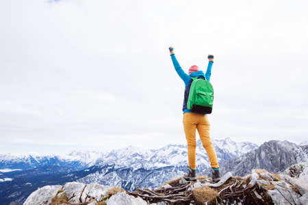 Female hiker with backpack raised her hands celebrating successful climb to top of mountainの写真素材